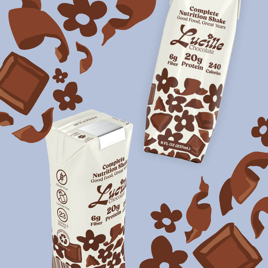 Two Lucille Chocolate Complete Nutrition Shake boxes with decorative chocolate pieces.