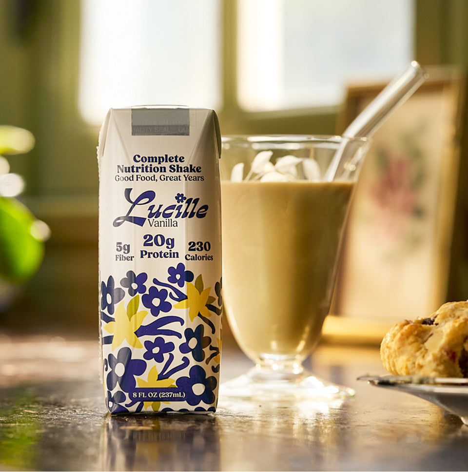 Lucille Vanilla Complete Nutrition Shake package with a glass of the shake.